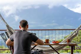 A man having breakfast at a balcony table, facing a forested mountain